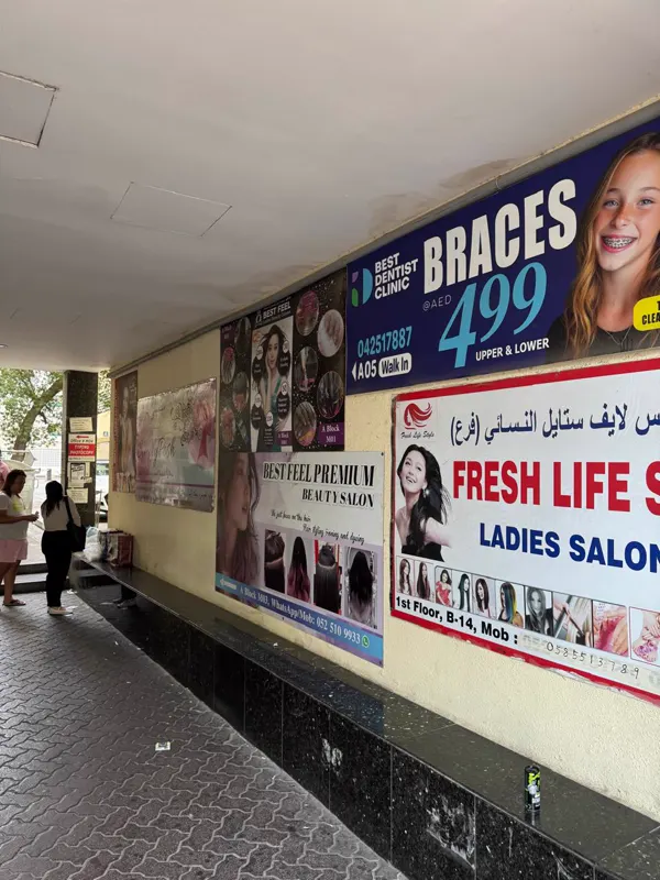 Covered walkway with clinic and salon posters beside the Al Owais Building